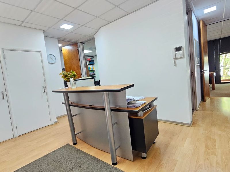 A professional office reception area featuring laminate flooring, a suspended ceiling with recessed lighting, and an integrated intercom system.