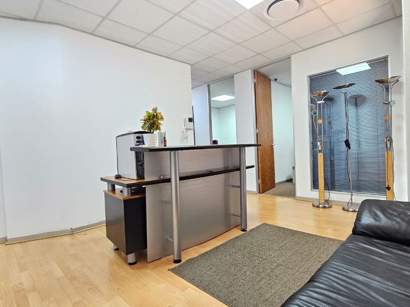 A functional office reception area featuring laminate flooring, a suspended ceiling, and internal glass partitioning for a professional workspace layout.