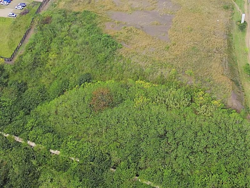 Aerial view of a vacant commercial land plot featuring natural vegetation, a paved turning circle, and perimeter fencing.
