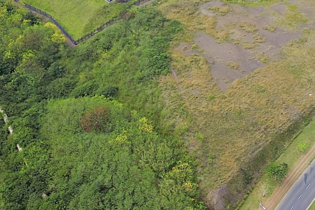 Aerial view of a vacant commercial land plot adjacent to an existing industrial park and main road access.