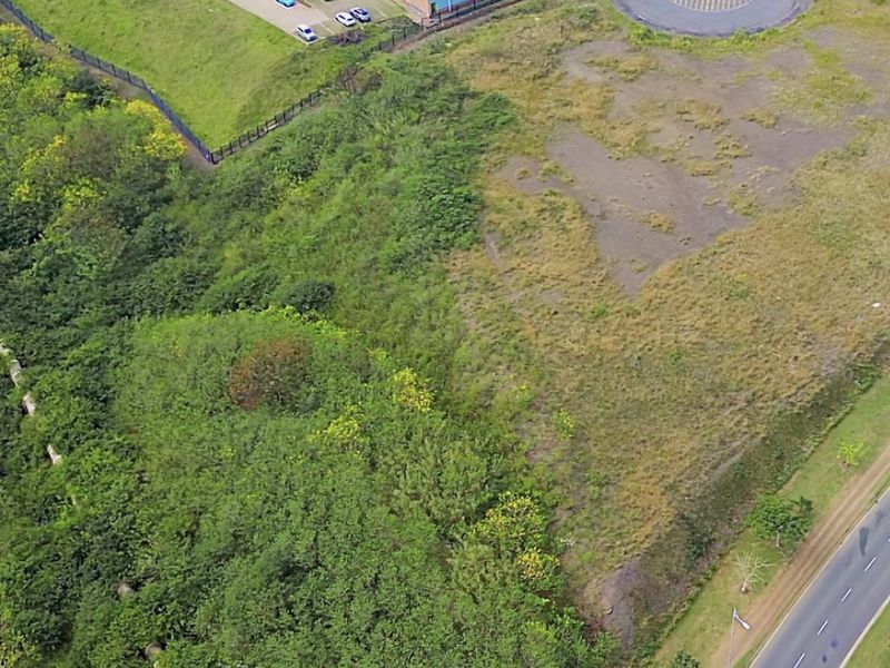 Aerial view of a vacant commercial land plot adjacent to an existing industrial park and main road access.