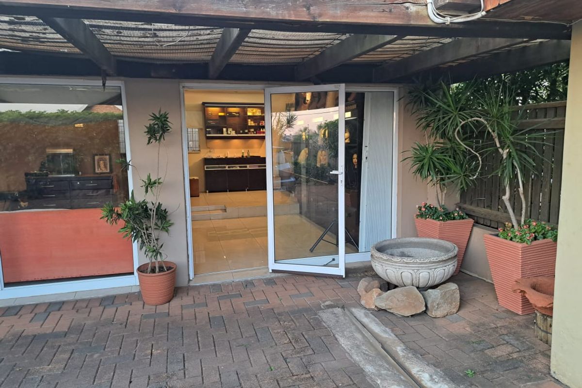 A covered outdoor patio area featuring a timber pergola, paved flooring, and direct access to the office interior through sliding glass doors.