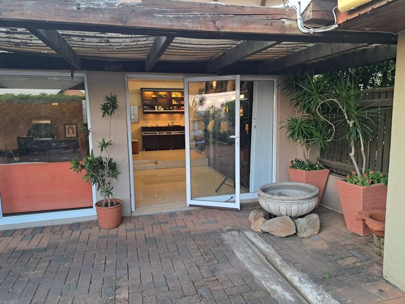 A covered outdoor patio area featuring a timber pergola, paved flooring, and direct access to the office interior through sliding glass doors.