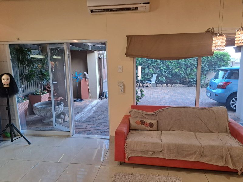 A bright living area featuring tiled floors, a split-system air conditioner, and large sliding glass doors providing direct access to an outdoor patio space.