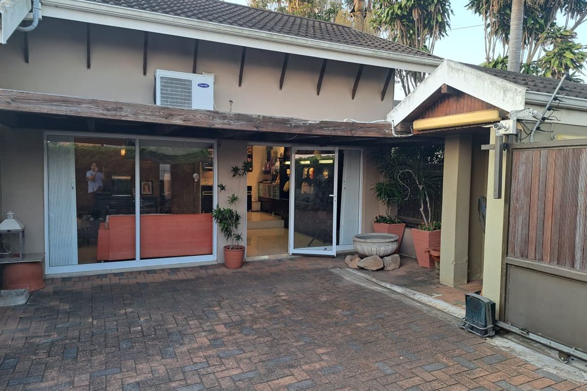 Rear exterior view of the office property featuring a paved courtyard, sliding glass access doors, and a timber pergola structure.