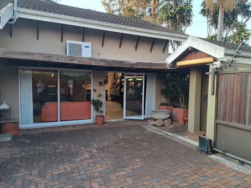 Rear exterior view of the office property featuring a paved courtyard, sliding glass access doors, and a timber pergola structure.