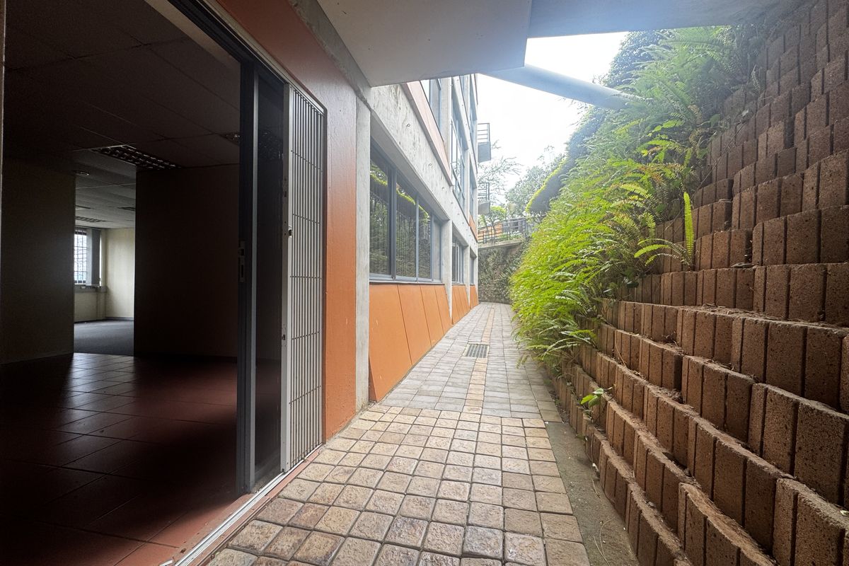 Exterior walkway featuring a paved path, retaining wall with greenery, and access to the office interior via a sliding glass door.