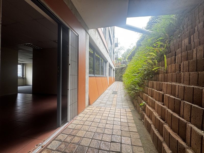 Exterior walkway featuring a paved path, retaining wall with greenery, and access to the office interior via a sliding glass door.