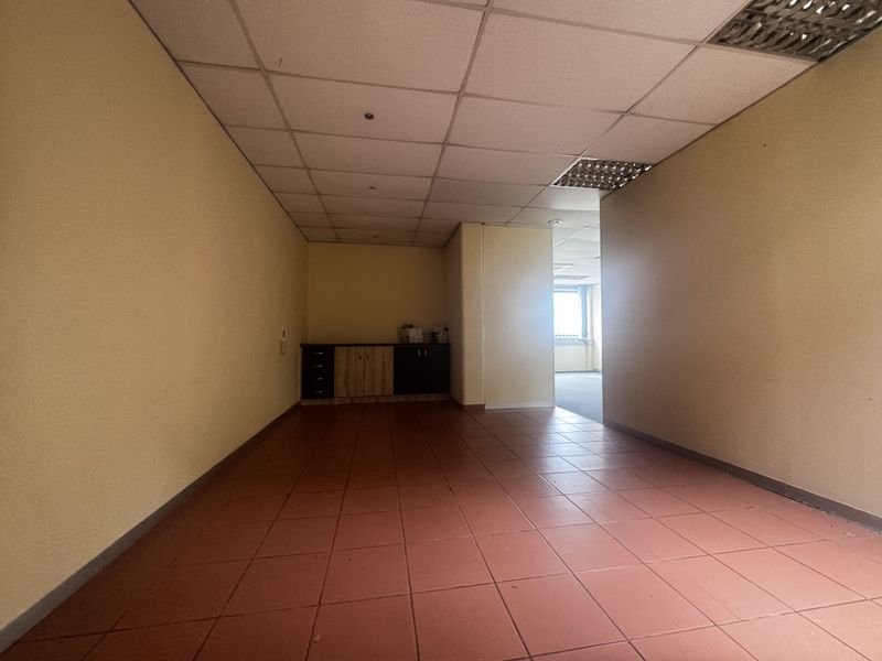 An empty office space featuring tiled flooring, a suspended ceiling with recessed lighting, and built-in cabinetry along the back wall.