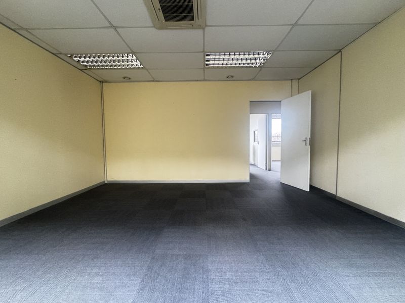 An empty office space featuring a suspended ceiling with recessed lighting, air conditioning, and dark carpet tiles.