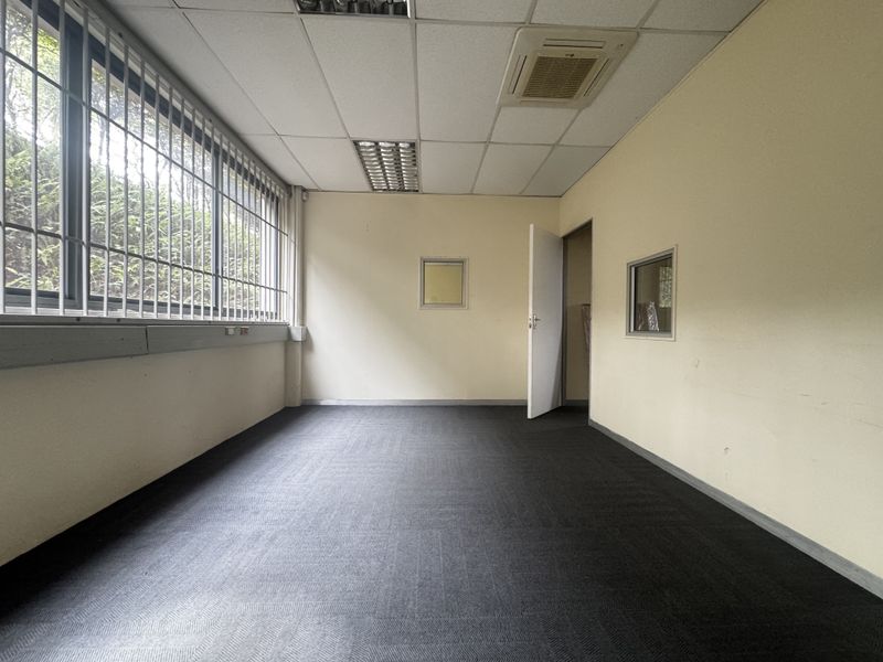 A vacant office space featuring carpeted flooring, a suspended ceiling with integrated lighting, ducted air conditioning, and security bars on the windows.