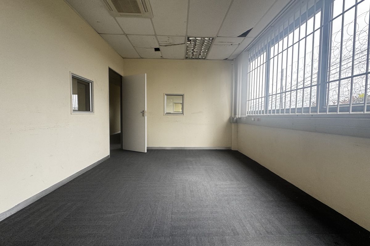 An empty office space featuring carpet flooring, suspended ceiling with recessed lighting, ducted air conditioning, and security bars on the windows.