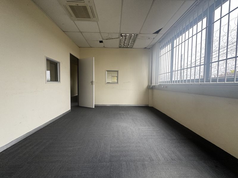 An empty office space featuring carpet flooring, suspended ceiling with recessed lighting, ducted air conditioning, and security bars on the windows.