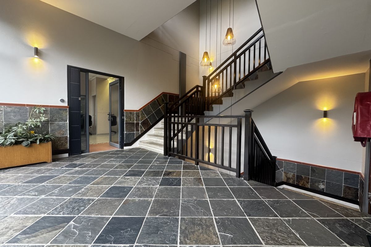 Spacious office building entrance foyer featuring slate tile flooring, a prominent wooden staircase, and modern wall and pendant lighting.