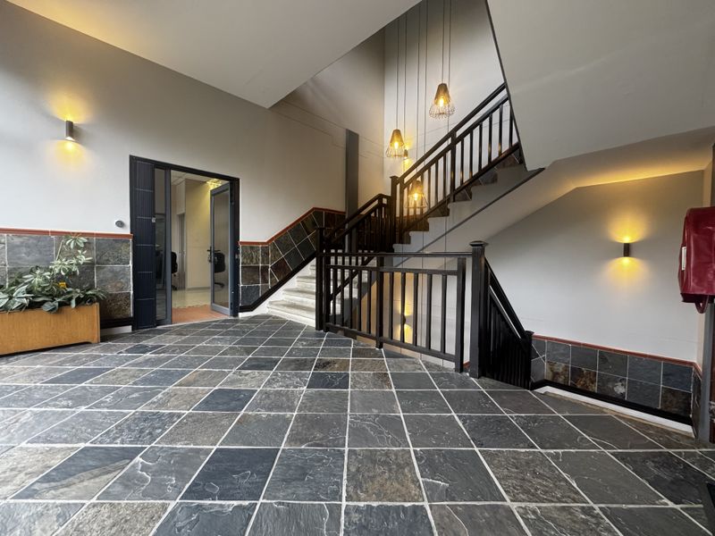 Spacious office building entrance foyer featuring slate tile flooring, a prominent wooden staircase, and modern wall and pendant lighting.