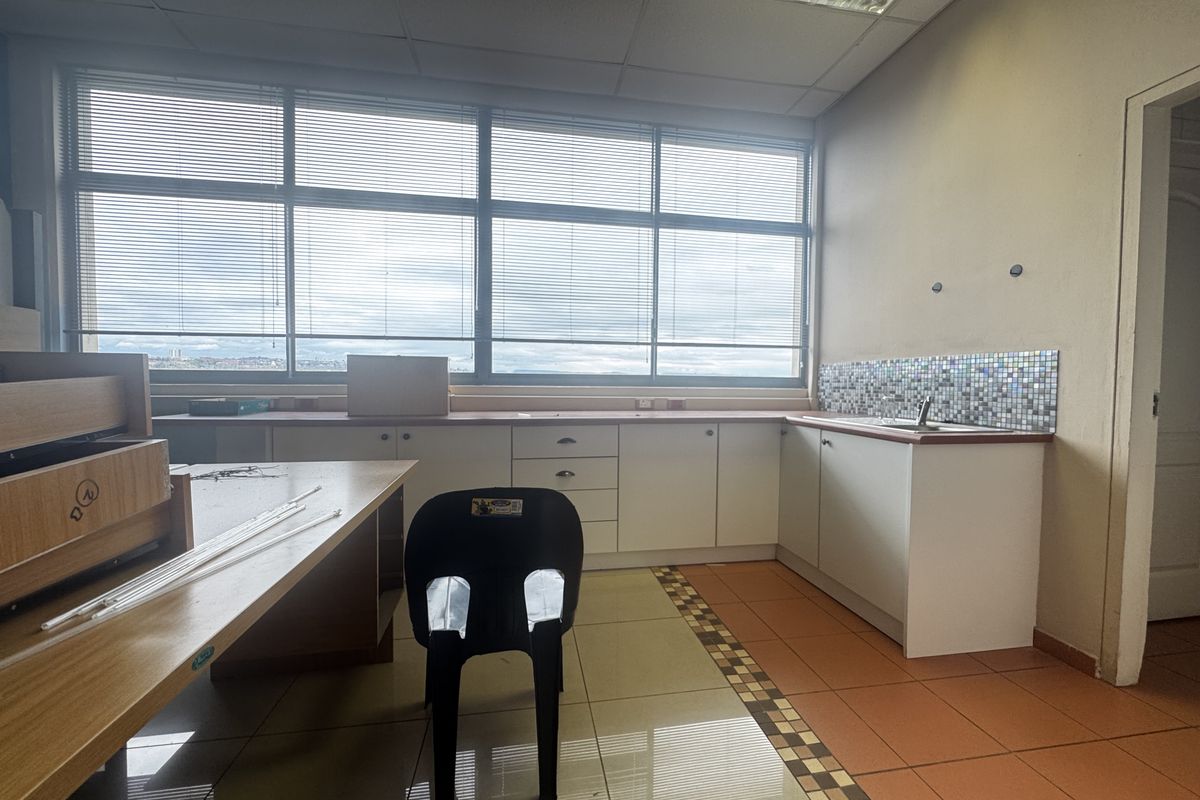A functional office kitchenette featuring built-in white cabinetry, a stainless steel sink, mosaic backsplash, and large windows with venetian blinds.