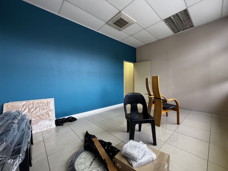 A functional office space featuring tiled flooring, a suspended ceiling with integrated air conditioning, and a bold blue accent wall.