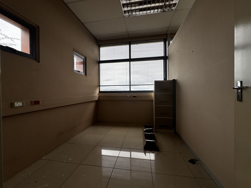 An empty office space featuring tiled flooring, suspended ceiling, and large windows with venetian blinds, suitable for a professional workspace.