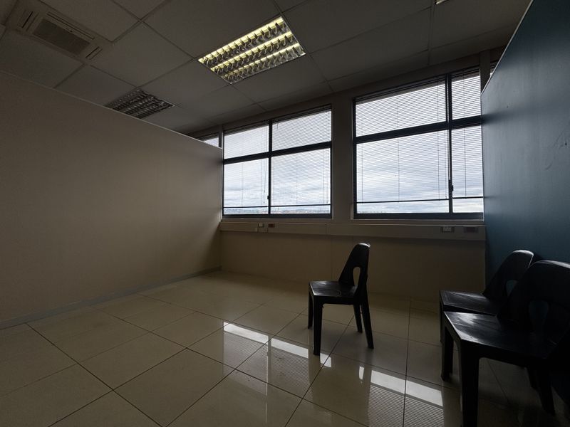 A vacant office space featuring tiled flooring, large windows with venetian blinds, and a suspended ceiling with integrated lighting.