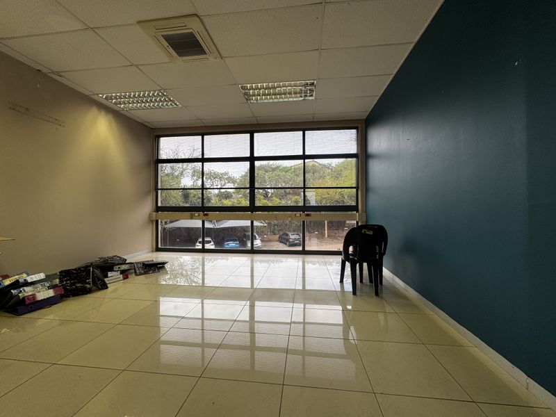 A spacious, empty office area featuring large windows, tiled flooring, and a suspended ceiling with integrated lighting and air conditioning.