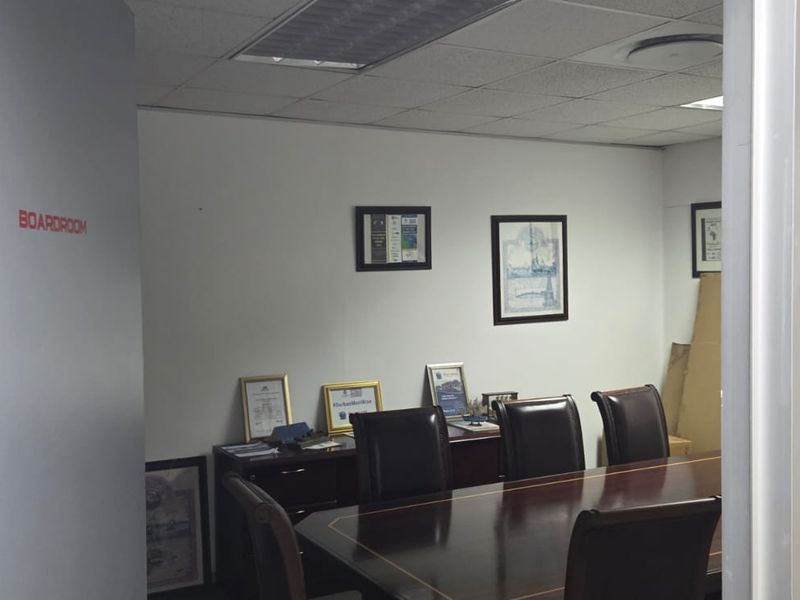 A functional office boardroom featuring a suspended ceiling, recessed lighting, and a frosted glass partition, providing a professional meeting environment.