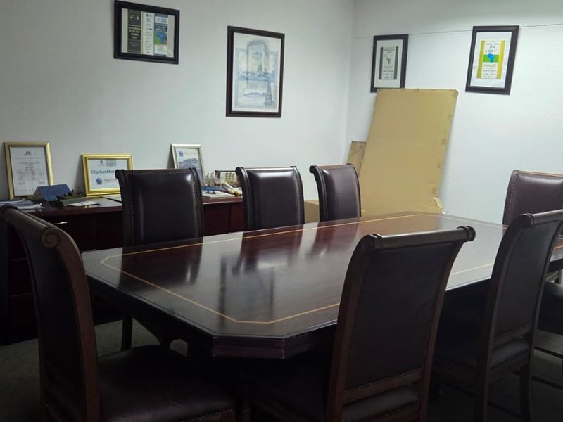 A functional office meeting room featuring a large boardroom table, carpeted flooring, and neutral wall finishes suitable for professional use.