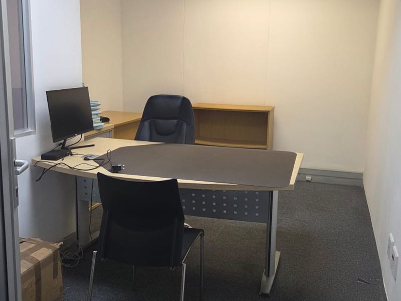 A functional office space featuring carpeted flooring and a glass partition door, providing a private work environment.