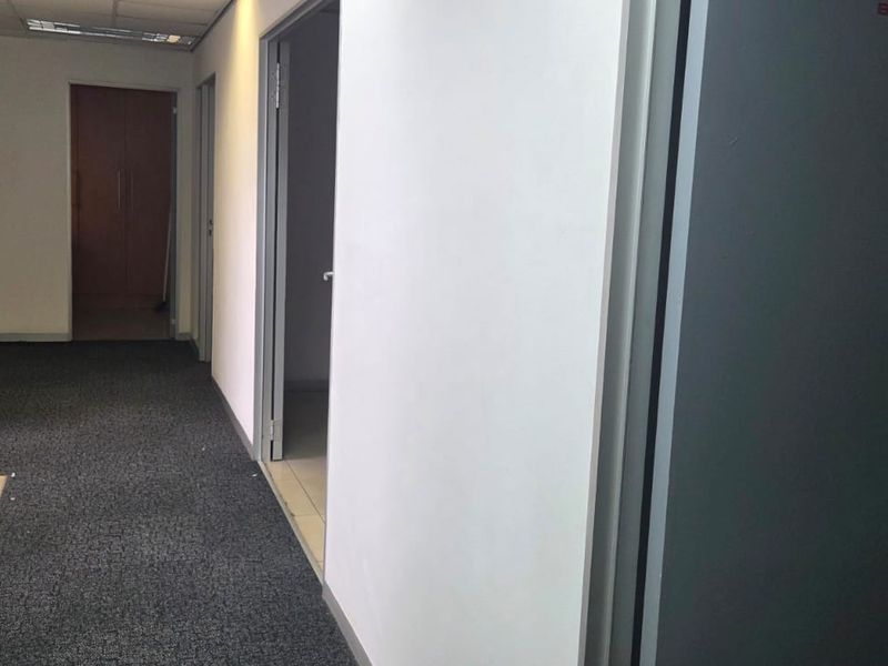 A functional office hallway featuring carpeted flooring, recessed ceiling lights, and access to multiple office rooms including a designated boardroom.