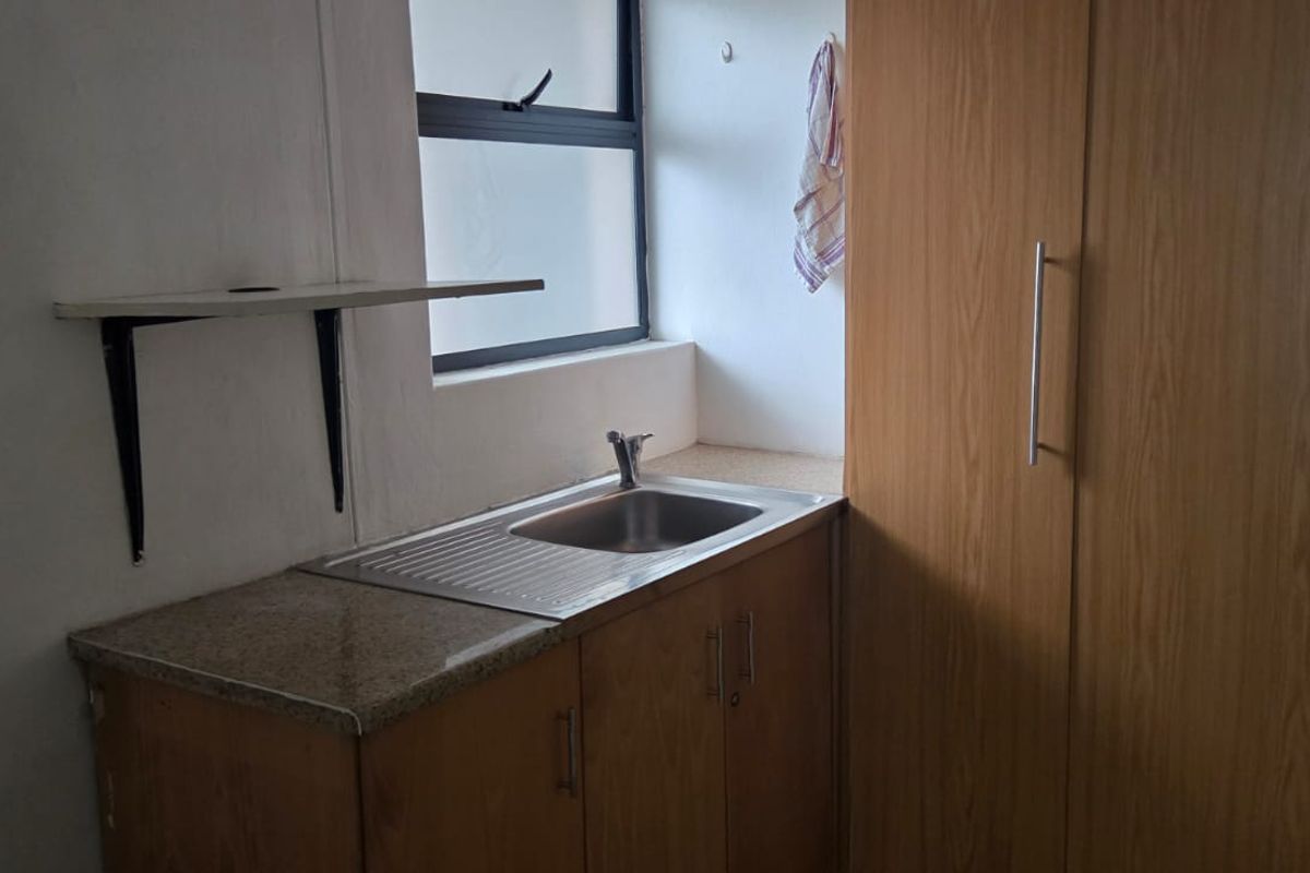 A compact office kitchenette featuring built-in wooden cabinetry, a stainless steel sink, and a laminate countertop.