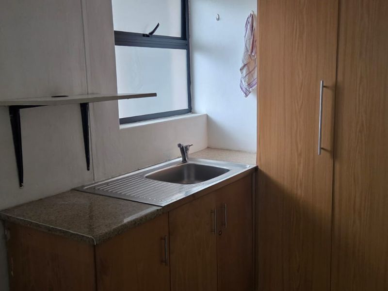 A compact office kitchenette featuring built-in wooden cabinetry, a stainless steel sink, and a laminate countertop.