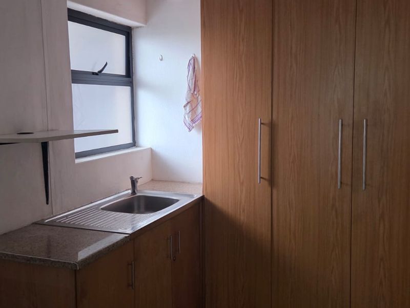 A functional scullery or utility area featuring built-in wooden cabinetry, a stainless steel sink, and a stone countertop.