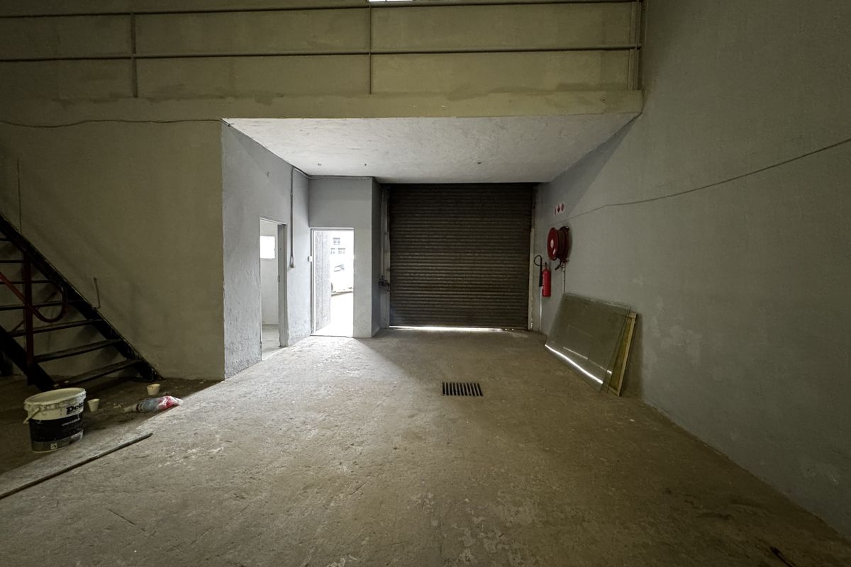 Industrial warehouse space featuring a roller shutter door, mezzanine level with metal staircase, and concrete flooring, suitable for storage or workshop use.