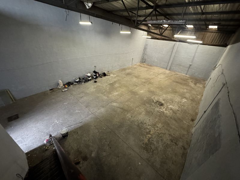 A spacious industrial utility area featuring exposed steel roof trusses, concrete flooring, and functional overhead fluorescent lighting, suitable for storage or workshop use.