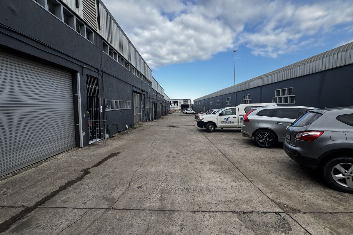 Exterior view of an industrial complex featuring a concrete driveway, multiple roller shutter doors, and secure access points.