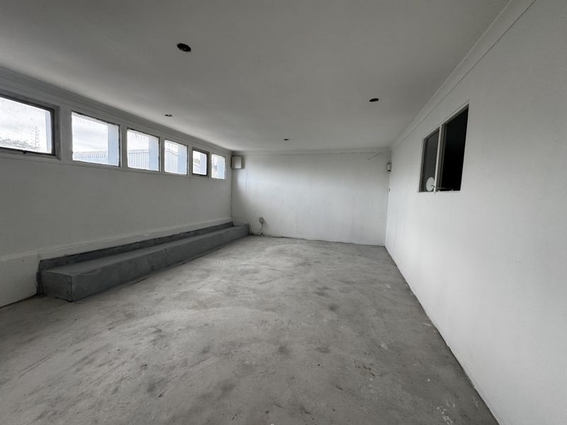 An empty, industrial-style utility space featuring a concrete floor, raised platform, and multiple windows providing natural light.