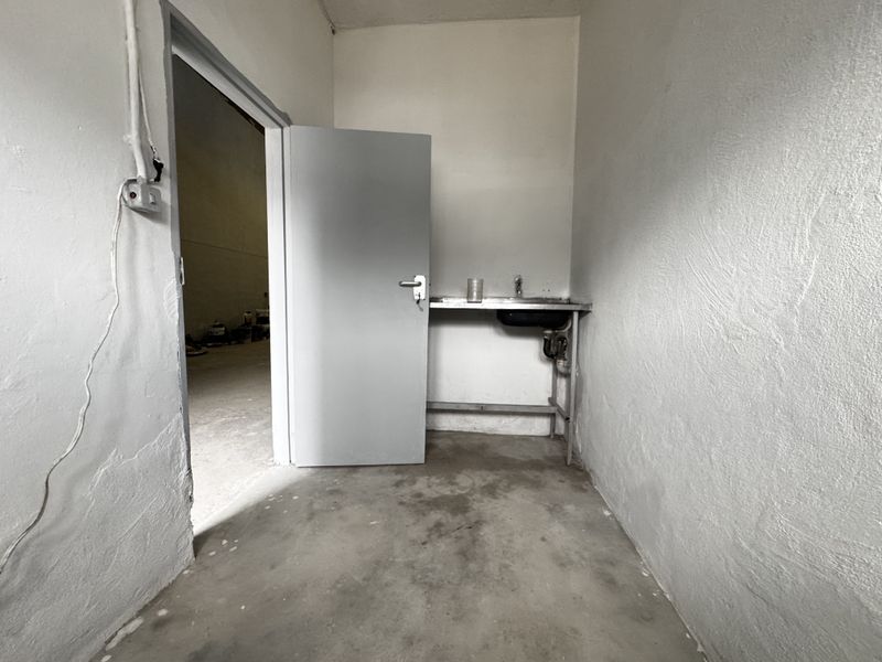 A small utility or scullery area featuring a basic stainless steel sink, exposed plumbing, and concrete flooring, suitable for industrial or workshop use.