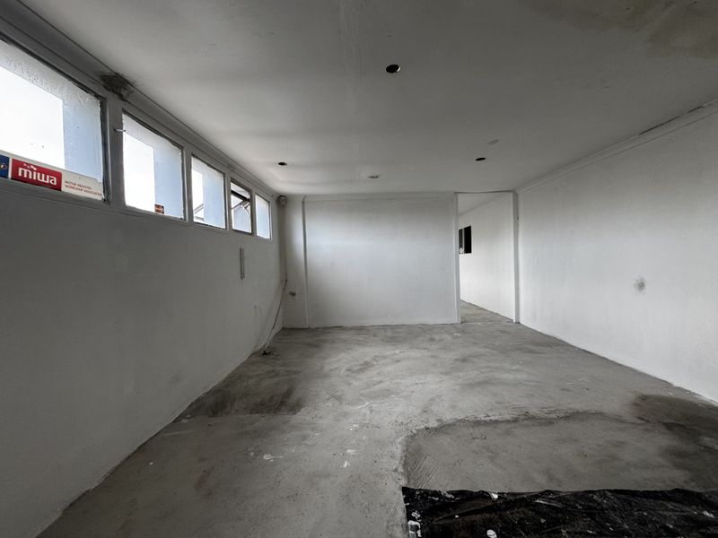 An empty, industrial-style utility space featuring concrete flooring, recessed lighting, and a row of casement windows along the side wall.