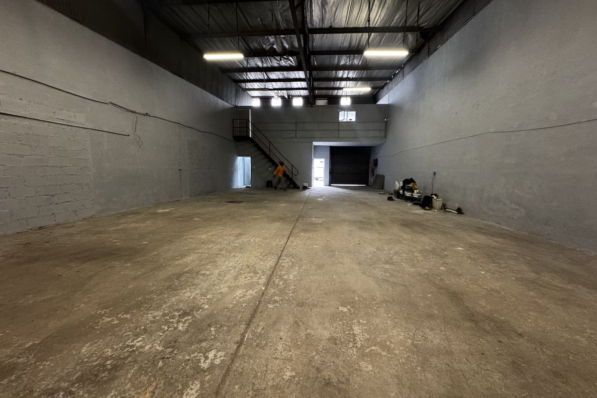 Spacious industrial warehouse unit featuring high ceilings, concrete flooring, a mezzanine level with staircase access, and a large roller shutter door for loading.