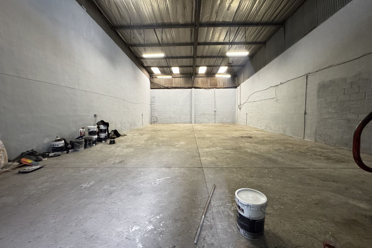 Spacious industrial warehouse unit featuring high ceilings with exposed steel trusses, concrete flooring, and functional overhead lighting.