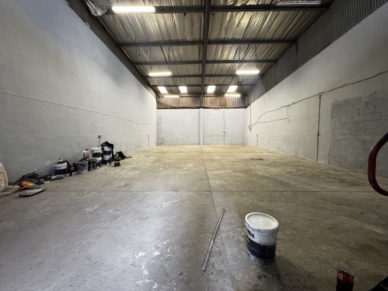 Spacious industrial warehouse unit featuring high ceilings with exposed steel trusses, concrete flooring, and functional overhead lighting.