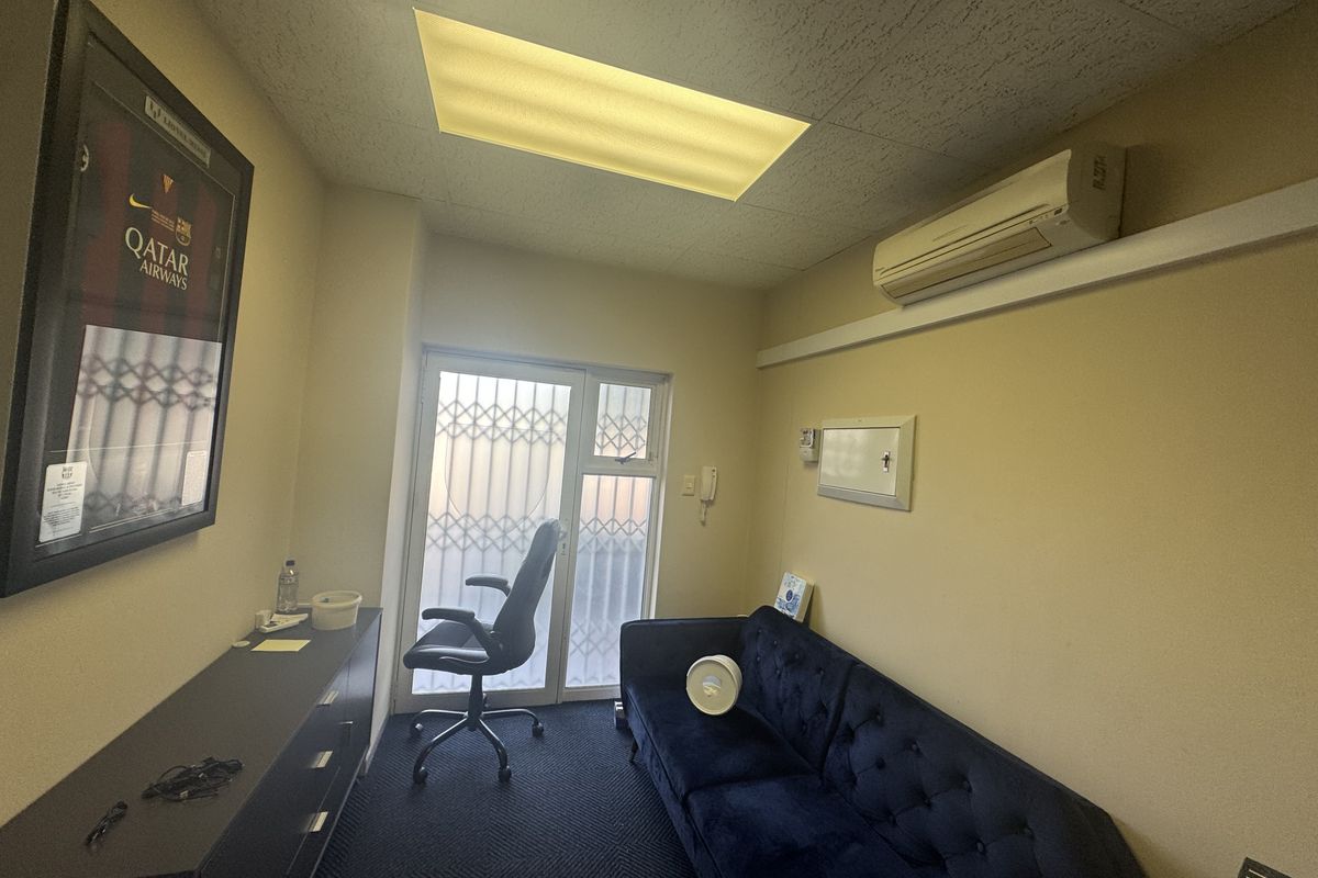 A compact office space featuring carpeted flooring, a drop ceiling with recessed lighting, and a wall-mounted split-system air conditioner.