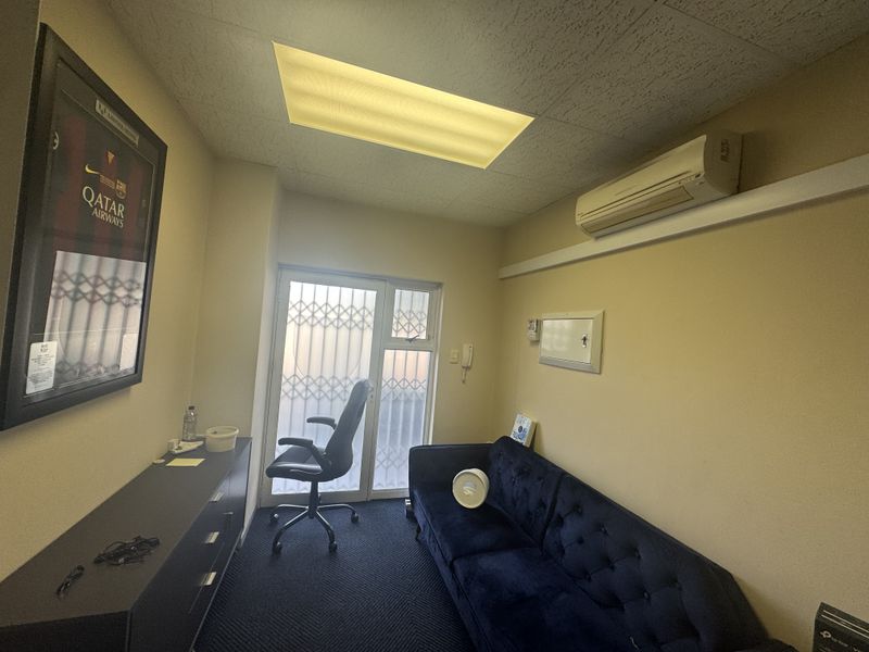 A compact office space featuring carpeted flooring, a drop ceiling with recessed lighting, and a wall-mounted split-system air conditioner.