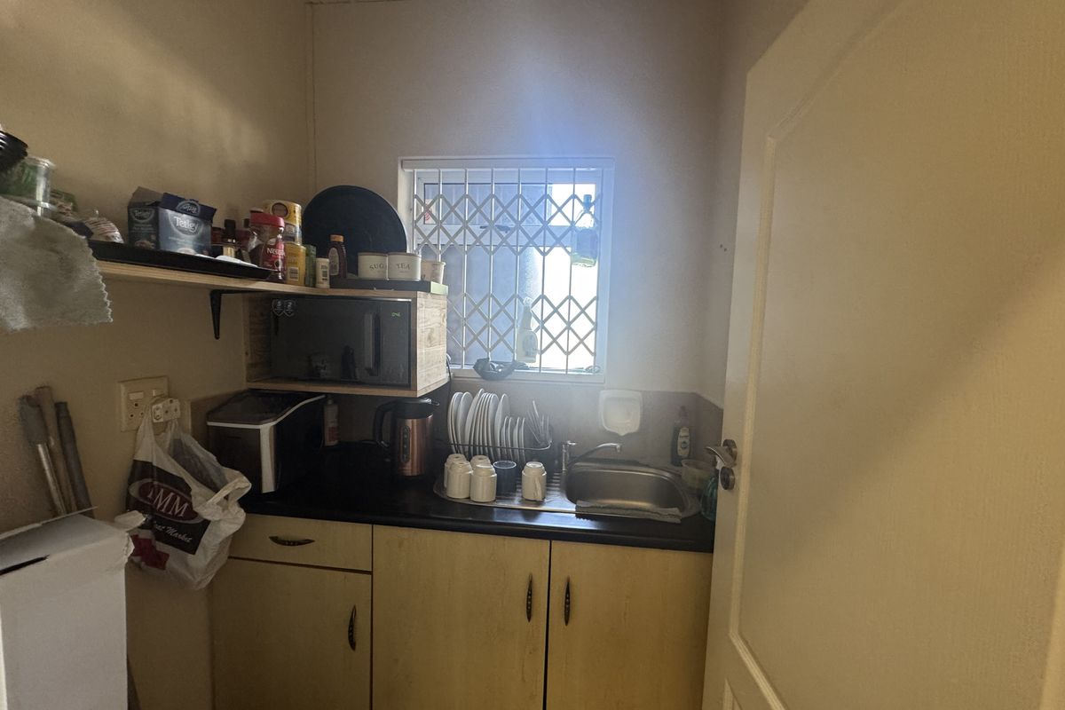 A compact scullery area featuring built-in cabinetry, a stainless steel sink, and a security-gated window, providing functional utility space.