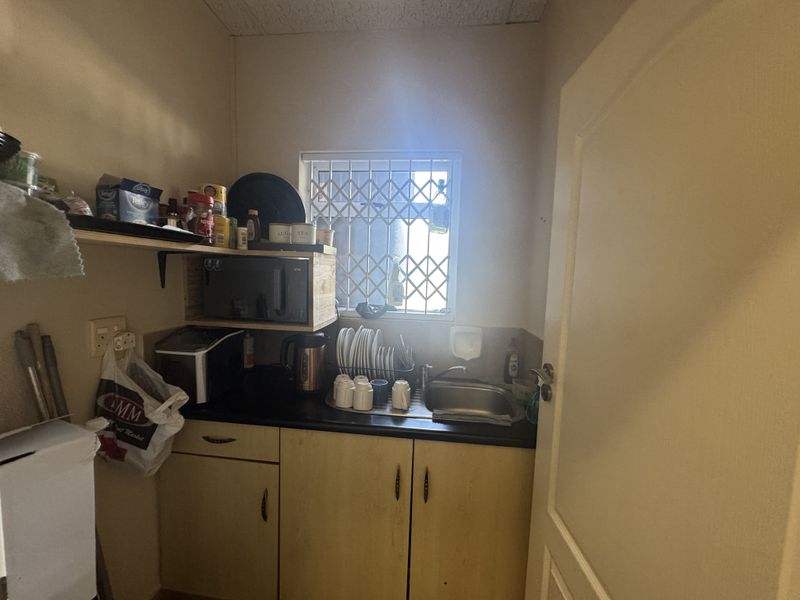 A compact scullery area featuring built-in cabinetry, a stainless steel sink, and a security-gated window, providing functional utility space.