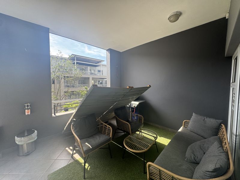 A covered balcony featuring tiled flooring, a metal safety railing, and a ceiling light fixture, offering an outdoor space for relaxation.