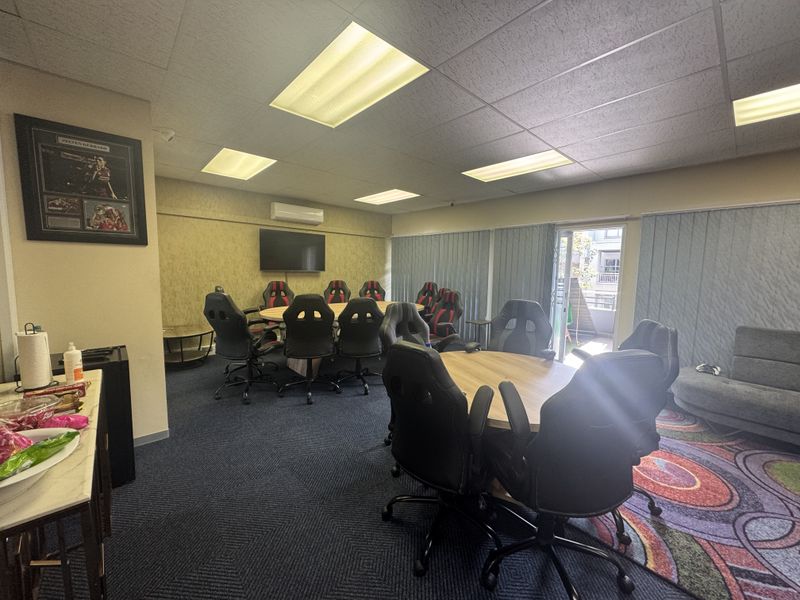 A functional office space featuring a suspended ceiling with recessed lighting, wall-mounted air conditioning, and access to an outdoor area via a sliding glass door.