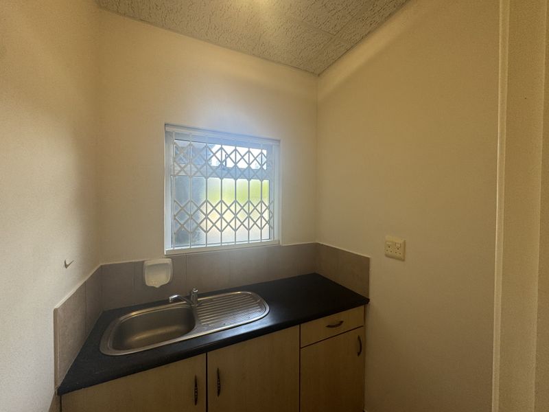 A functional scullery or utility area featuring a stainless steel sink, laminate countertop, built-in cabinetry, and a window with a security gate.