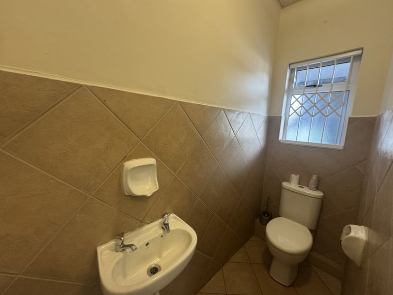 A compact office restroom featuring a pedestal washbasin, toilet, and diamond-patterned ceramic wall tiling with a security-barred window.