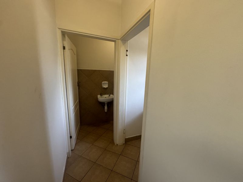 A functional hallway area leading to a small washroom featuring tiled flooring and a wall-mounted basin.