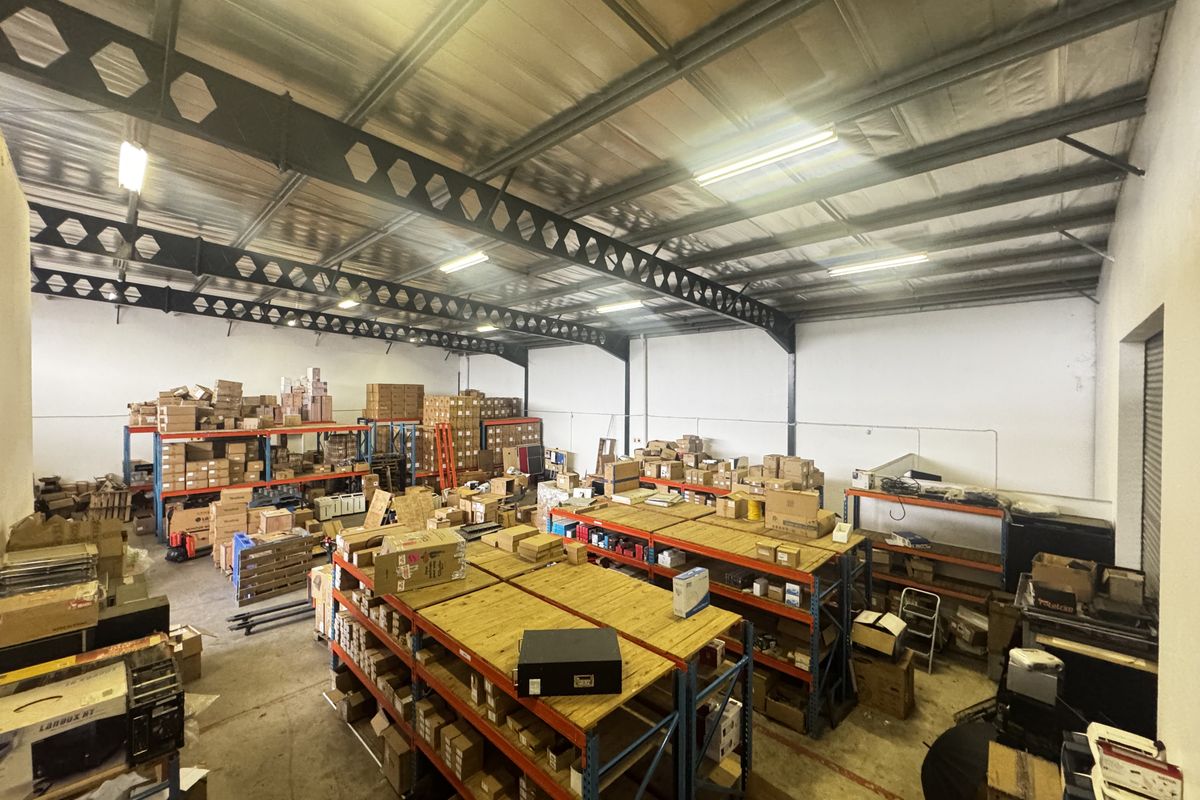 Spacious industrial warehouse area featuring high ceilings with exposed steel trusses, concrete flooring, and extensive built-in metal racking for storage.